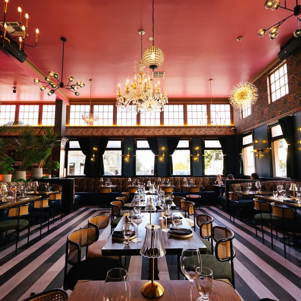 Luxurious restaurant dining room featuring a red ceiling, striped floor, chandeliers, and plush seating.