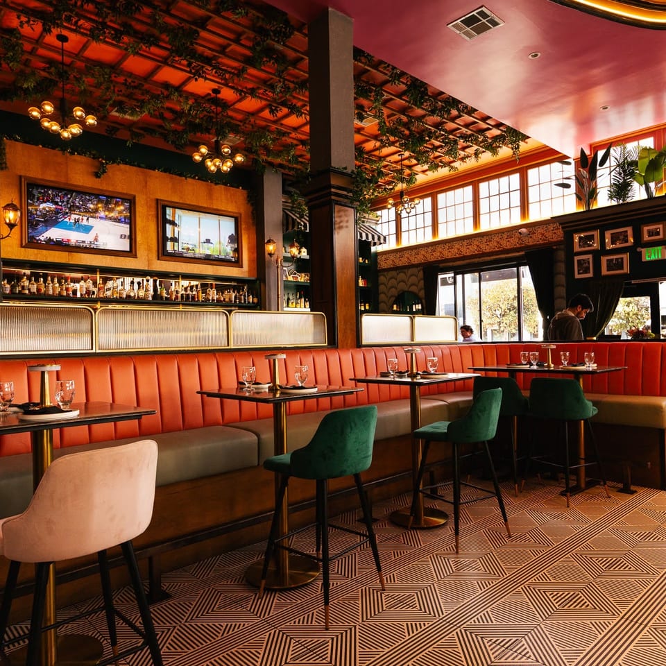 Vibrant restaurant interior with orange booths, bar stools, a full bar, and geometric patterned floor.