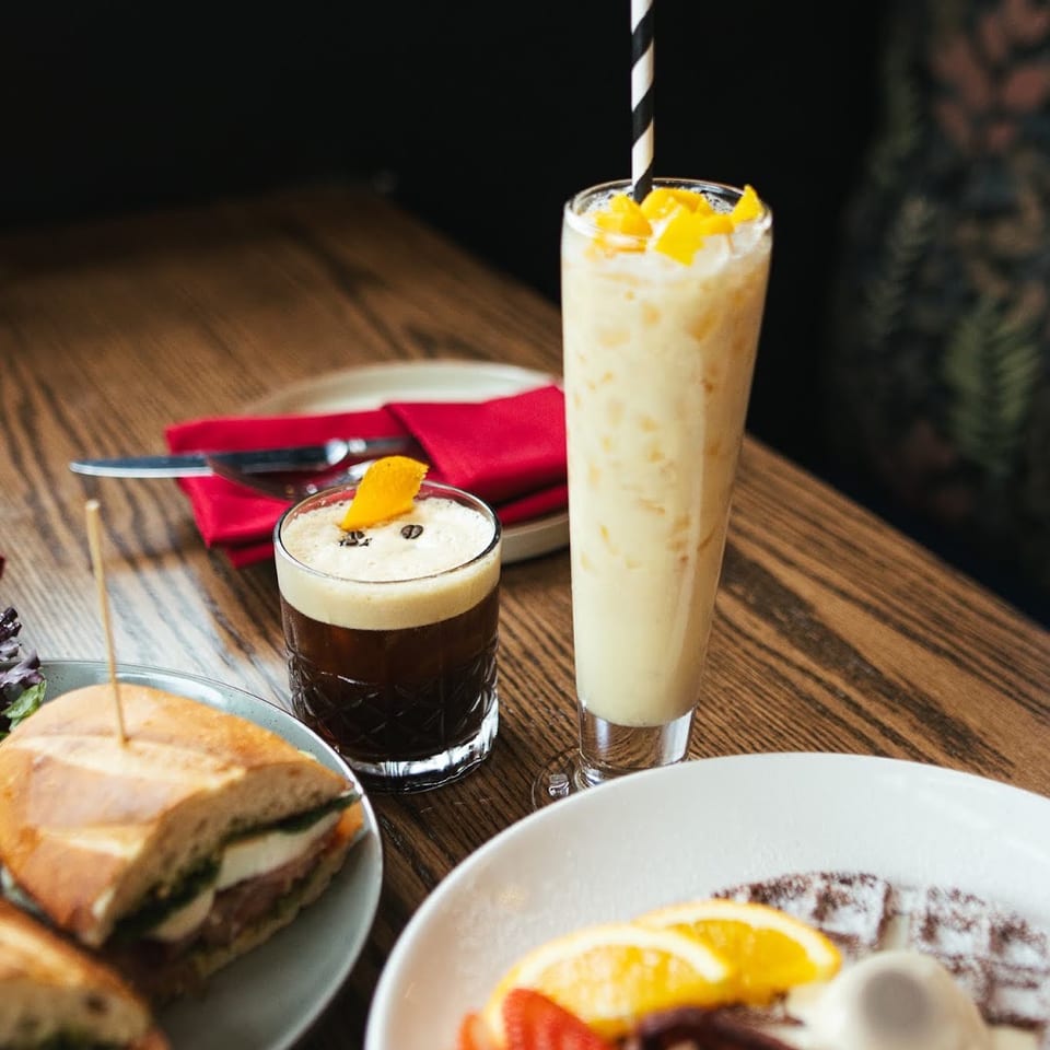 Delicious breakfast spread with a sandwich, waffle, espresso martini, and mango smoothie on a wooden table.