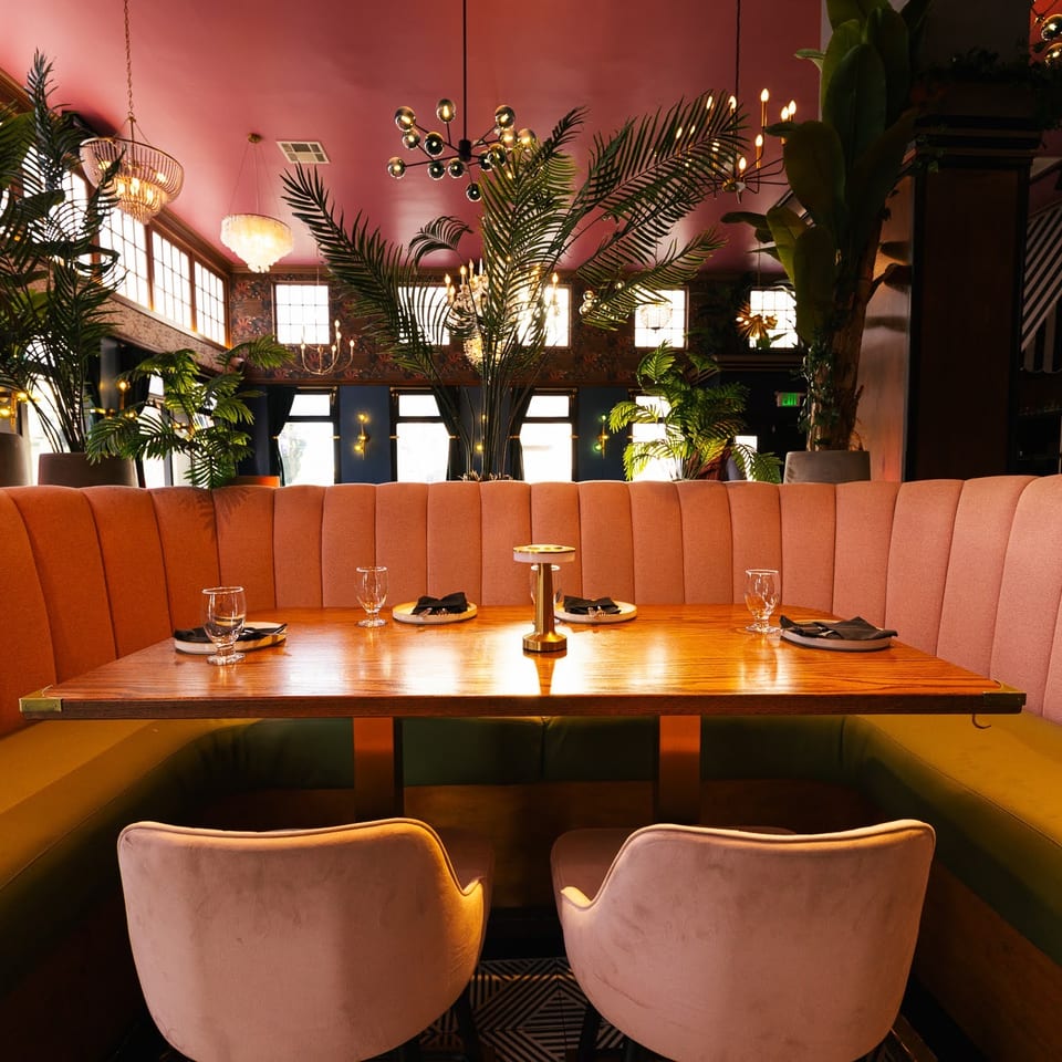 Vibrant restaurant interior with a pink and green booth, wooden table, and lush plants.